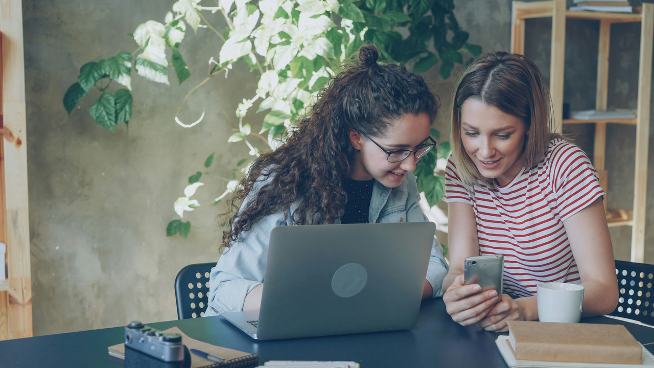 Two teenage girl entrepreneurs working in front of a laptop and phone