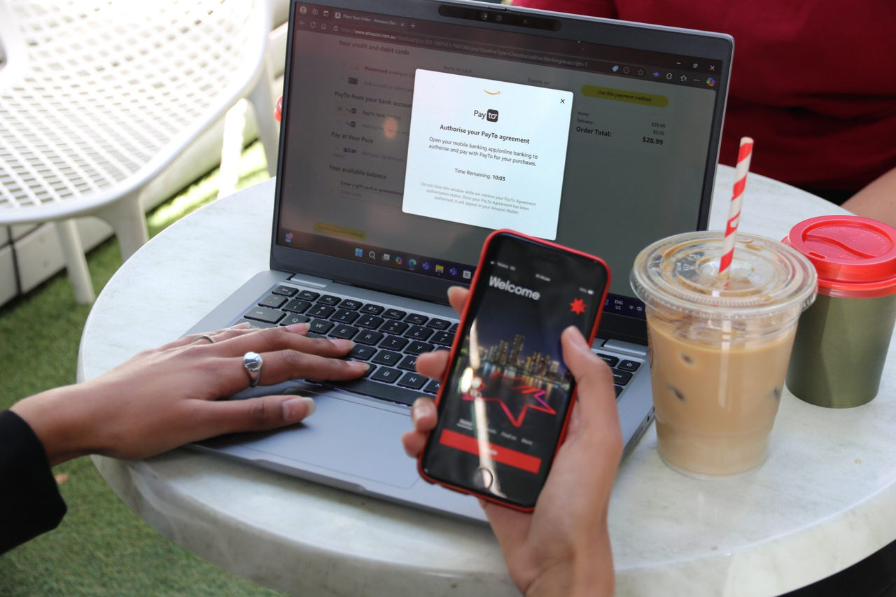 hand holding mobile phone with other hand on laptop