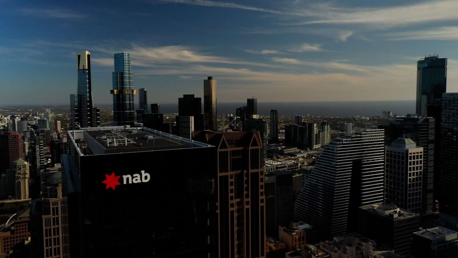 An aerial view displaying the NAB Melbourne building with the city skyline in the background, featuring other buildings.