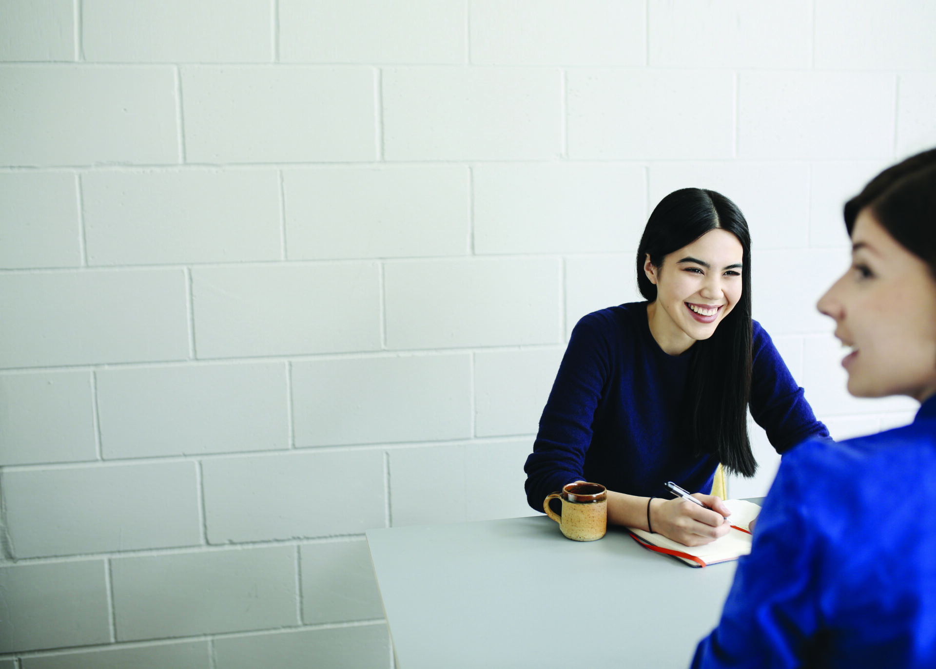 young woman at desk, smiling and writing notes