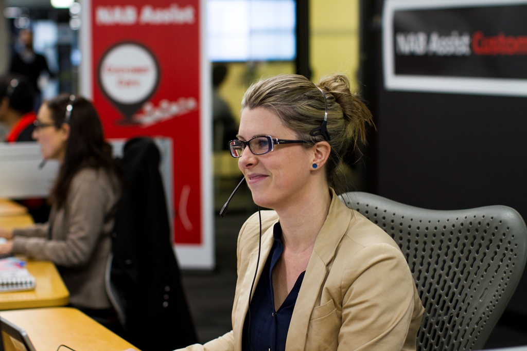 Photograph of a woman with a headset in an office with a NAB Assist banner in the background.