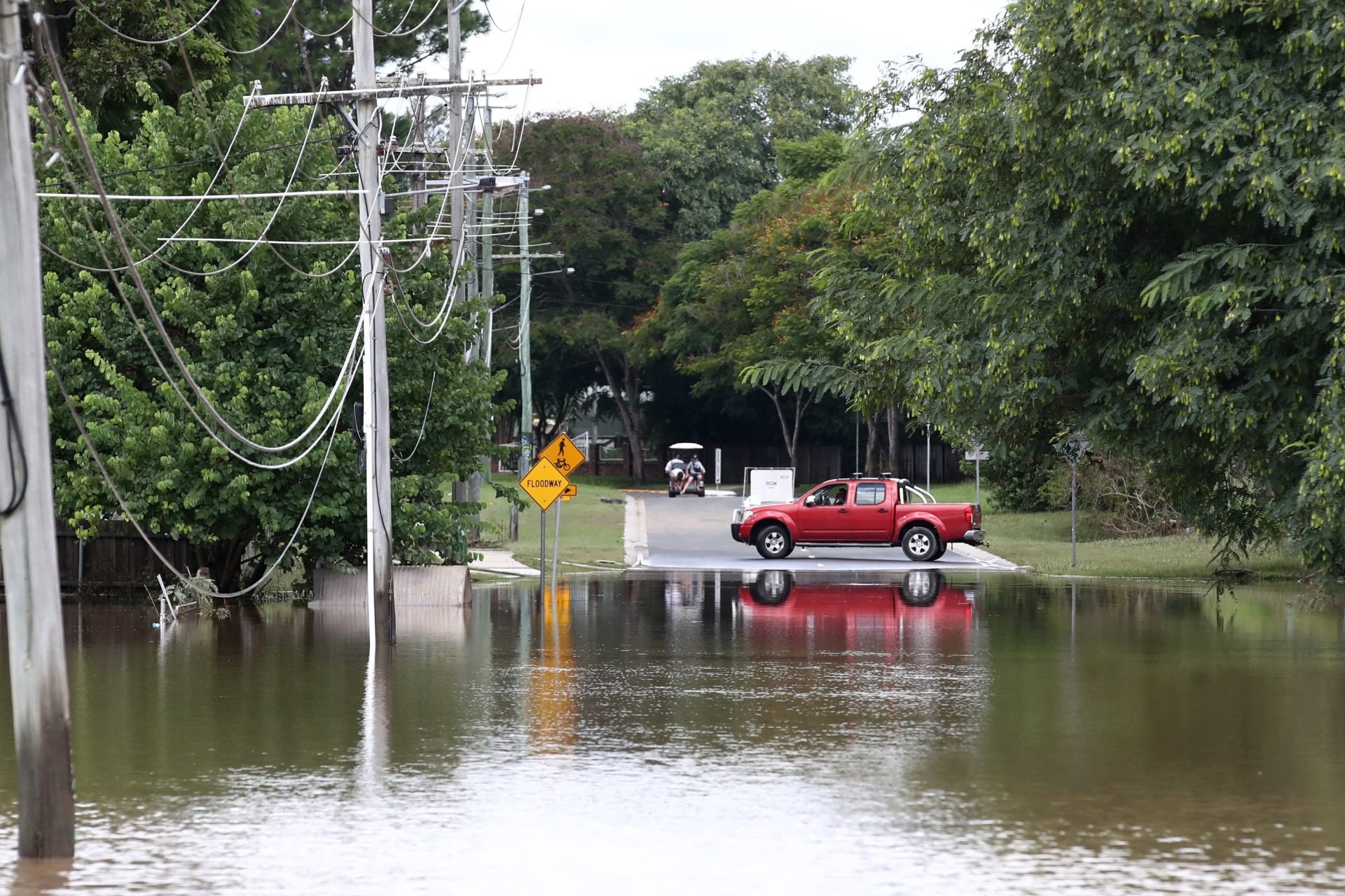 Flooded road with red car parked next to the water near a sign saying "Flood"