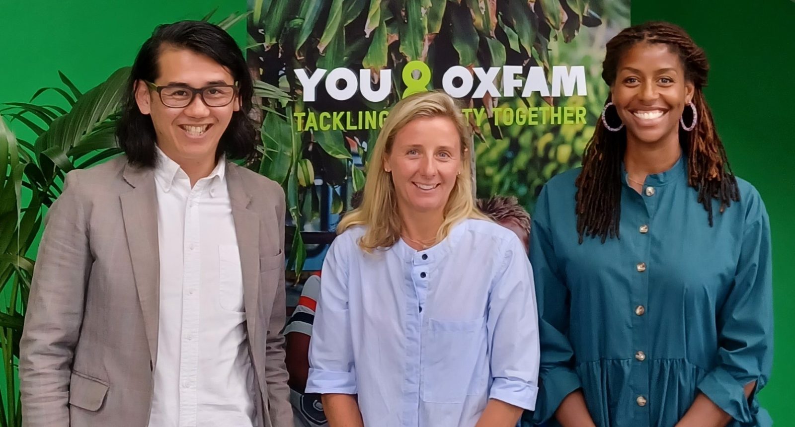 A man and two women all smiling in front of an Oxfam poster