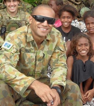 Brian Wyborn in military uniform surrounded by children and soldiers in the Solomon Islands