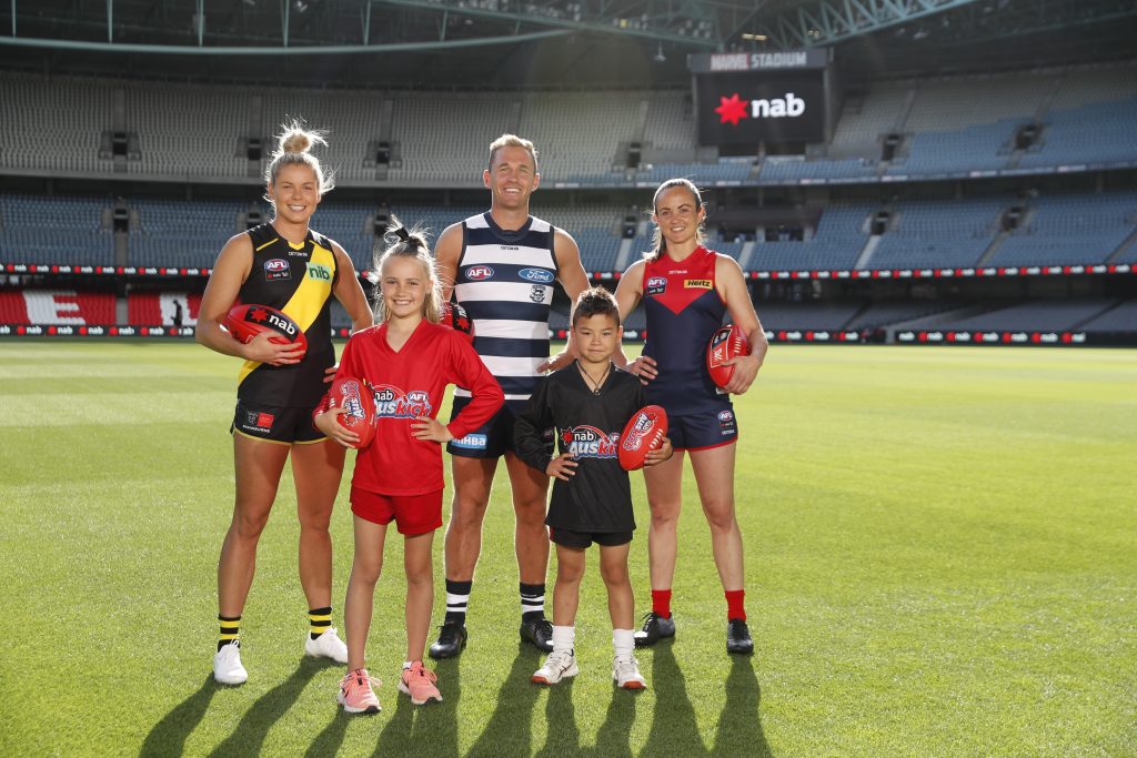 Image of two children with an AFL Men's player and two AFLW players on the ground at Marvel Stadium.