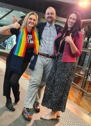 Three people standing in a building smiling.