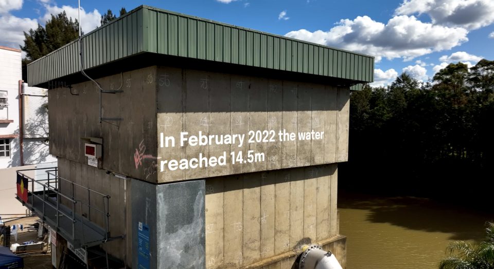 A photo of a concrete structure with writing on it that reads 'In February 2022, the water reached 14.5 metres.' There is a river in the background.
