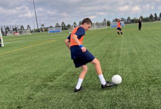 A boy kicks a soccer ball on the oval