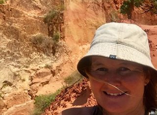 A lady wearing a hat smiles in bright sun.