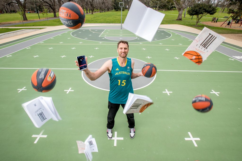 Man on basketball court juggling a phone, books and basketballs