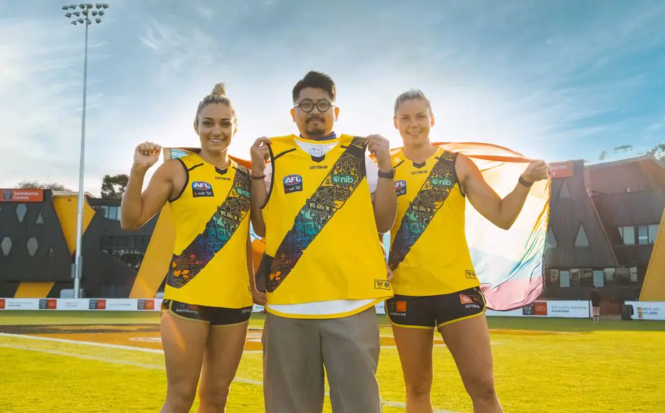 Katie Brennan holding the Richmond Tigers pride guernsey, standing on a footy oval