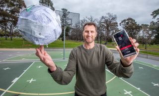 Man spinning basketball covered in receipts on one hand and holding a phone in the other