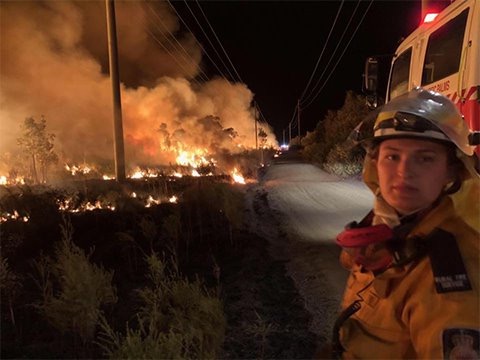 A volunteer firefighter stands in front of bushfires.