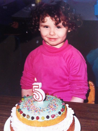 Young Megan standing behind a cake with a '5' candle