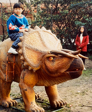 Young girl - Enqi Xu - sitting on a dinosaur statue