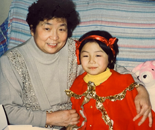 A young girl - Enqi - sitting on a sofa, embraced by her grandma