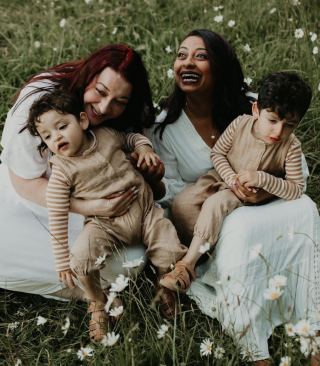 Family photo of two women in wedding dresses sitting on grass with their two sons