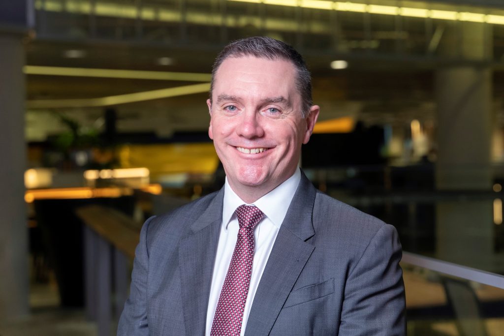 Image of a man in a suit and tie smiling.