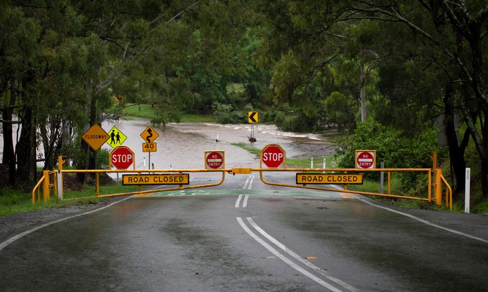 A road blocked by flood waters with stop signs and road closed signs.