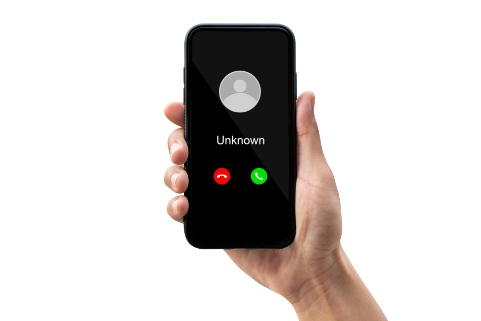 Image of a hand holding a phone with the screen showing an unknown number and a red and a green button.