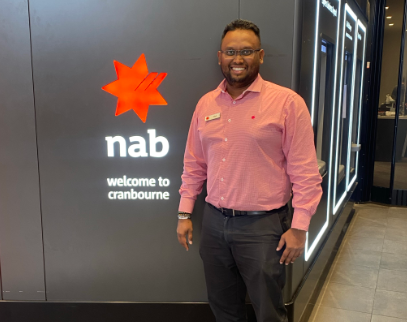 NAB banker in red shirt standing in front of a block wall displaying a NAB logo