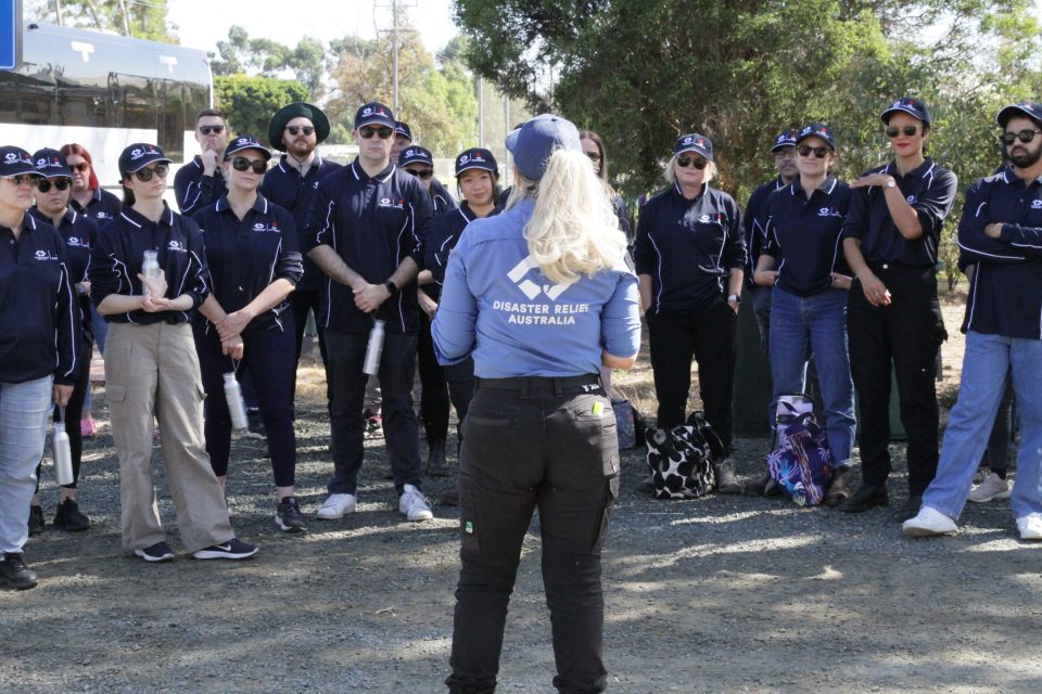 Volunteers from NAB standing in semi-circle listening to Disaster Relief Australia briefing