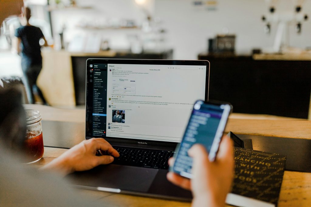 Person at a computer holding a phone in one hand.