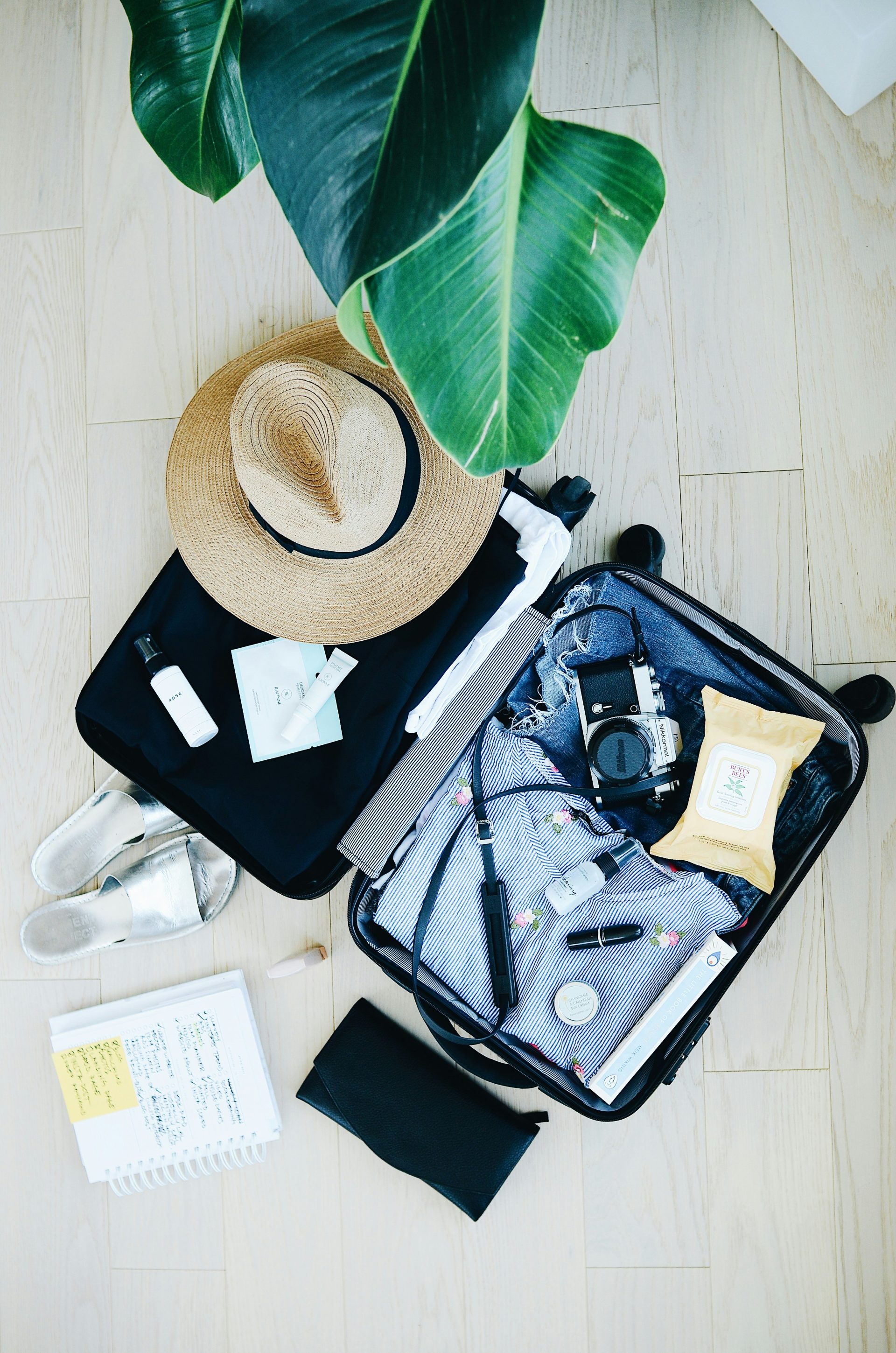 Flat lay image of suitcase and travel items like a hat and sunglasses