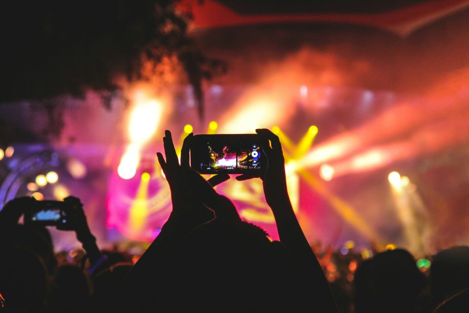 Image of people at a concert with mobile phones held up and bright stage lights.
