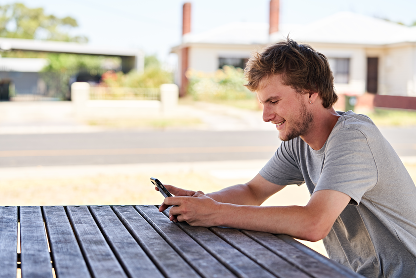 A young man sitting at a bench., looking at his phone