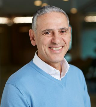 Headshot of Pacific Blue Chief Executive Domenic Capomolla wearing a white shirt and blue sweater smiling at the camera