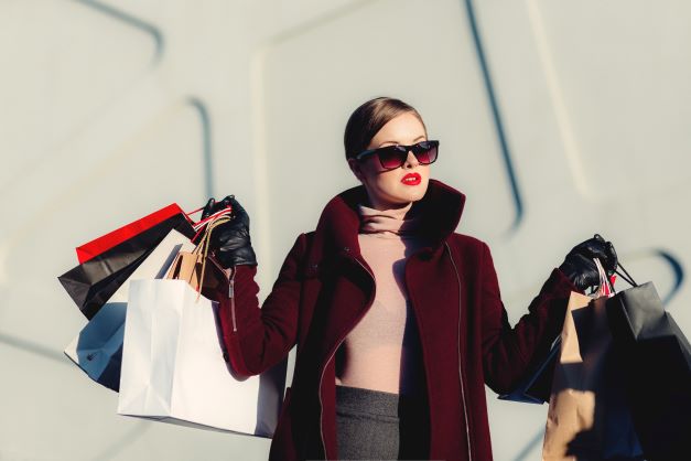 women in dark red coat with sunglasses and arms full of shopping bags