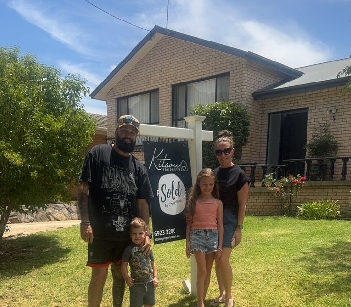 Family standing infront of sold sign and house