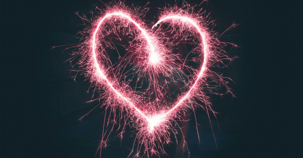 A pink love heart shape with a sparklers effect on a black background.