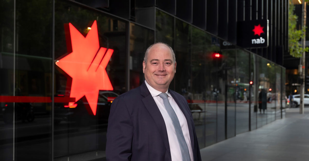 Man in a blue suit and white shirt standing in front of a black building with red star.
