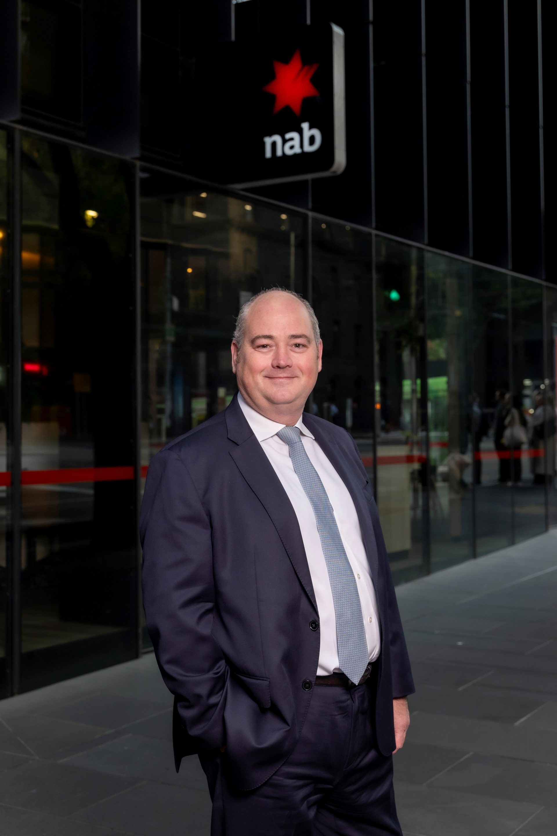 A man in a suit standing in front of a bank branch